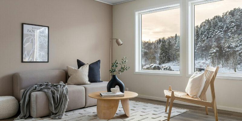 Salon lumineux et confortable avec grandes fenêtres offrant une vue sur un paysage enneigé, illustrant l'importance de l'isolation thermique et du confort de la maison avant l'hiver.
