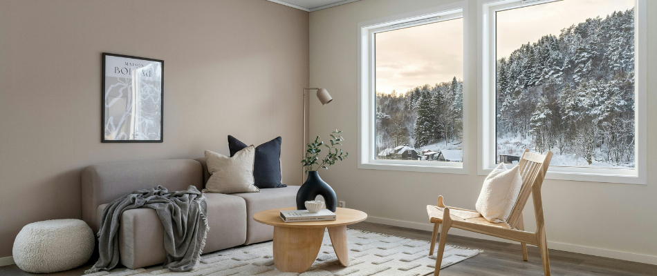 Salon lumineux et confortable avec grandes fenêtres offrant une vue sur un paysage enneigé, illustrant l'importance de l'isolation thermique et du confort de la maison avant l'hiver.